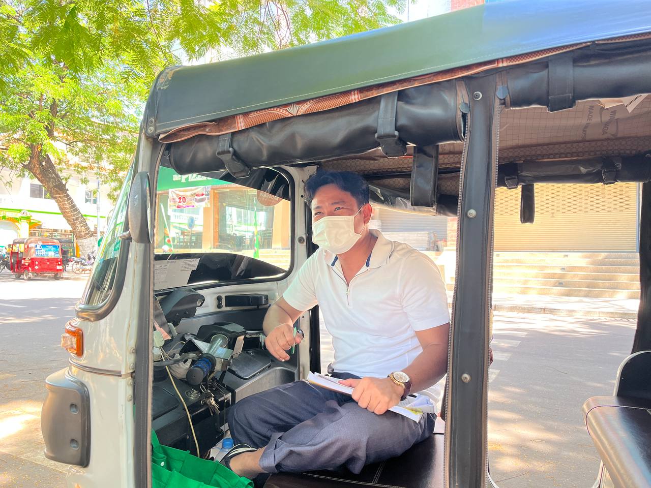 លោក ហេង សុភាព​&nbsp;ចតម៉ូតូកង់បីឥណ្ឌាក្រោមដើមឈើអង្គុយកត់របាយការណ៍ចំណូលប្រចាំថ្ងៃ។ រូបភាព៖ ឃ្លាំង គីមហួយ